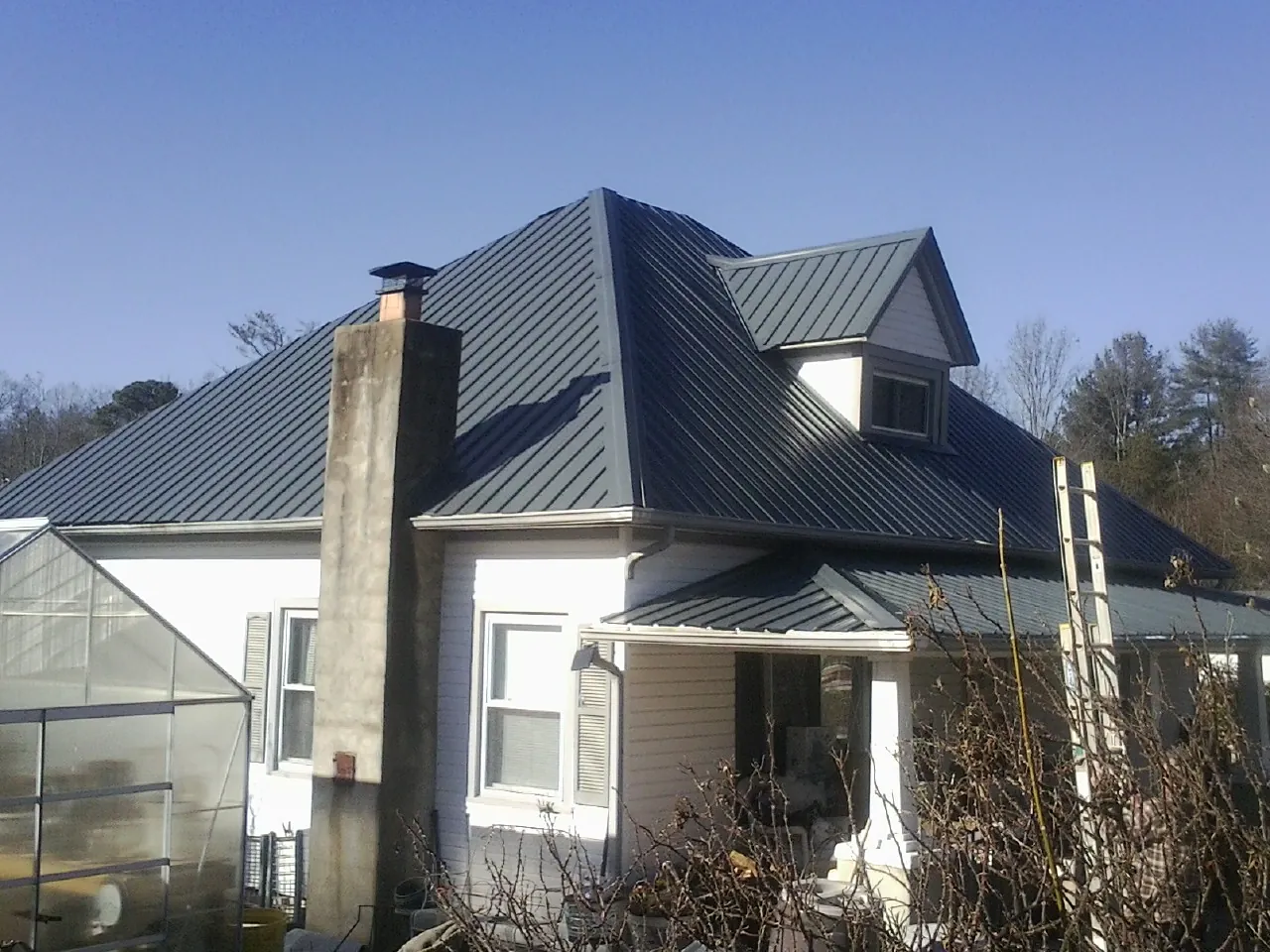 Dark blue standing seam metal roof on a white farmhouse with dormer — Slate & Tile Roof Repair by Roofing Brothers in Rillton