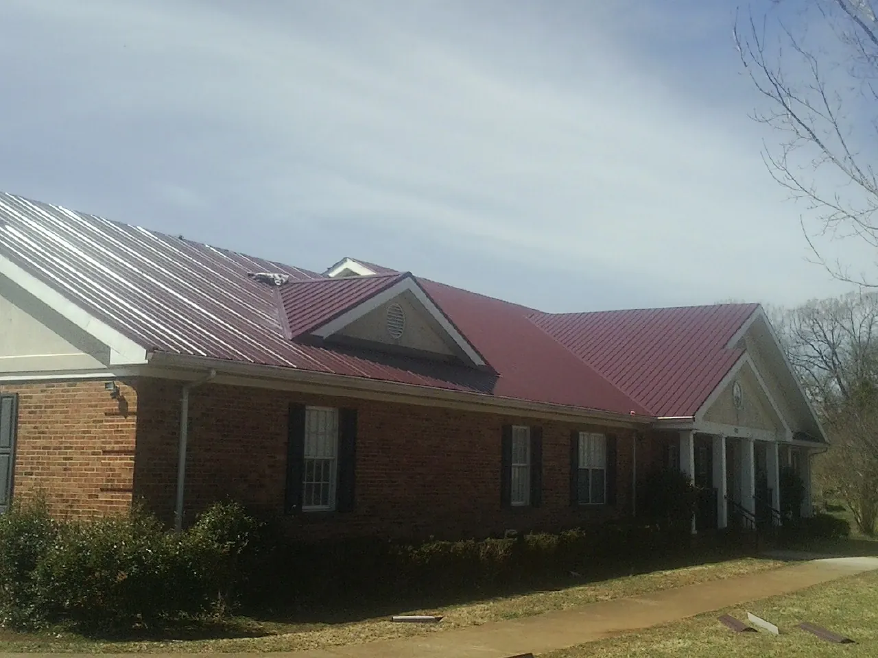 Red metal roof with gabled entries on a long brick building, from a Hail Damage Roof Repair job in Rillton
