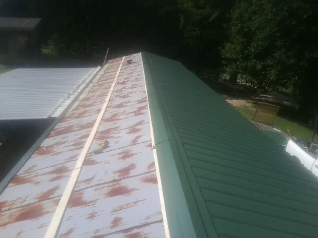 Old rusted panels beside newly installed green metal roofing — Wind Damage Roof Repair by Roofing Brothers in Rillton
