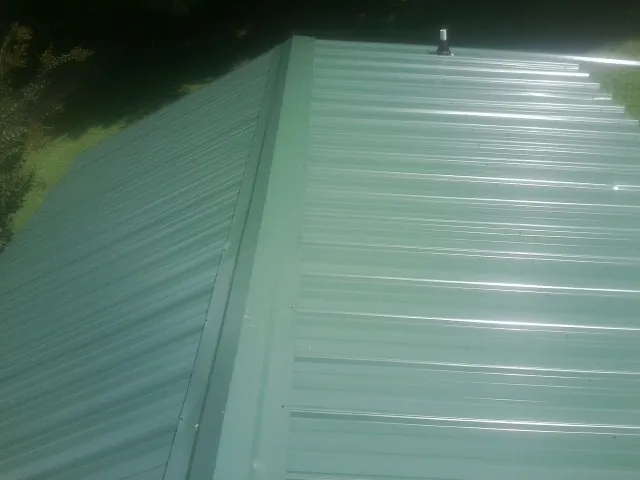 New green metal panels meeting at the ridge of a roof — Flat Roof Repair work by our crew in Rillton