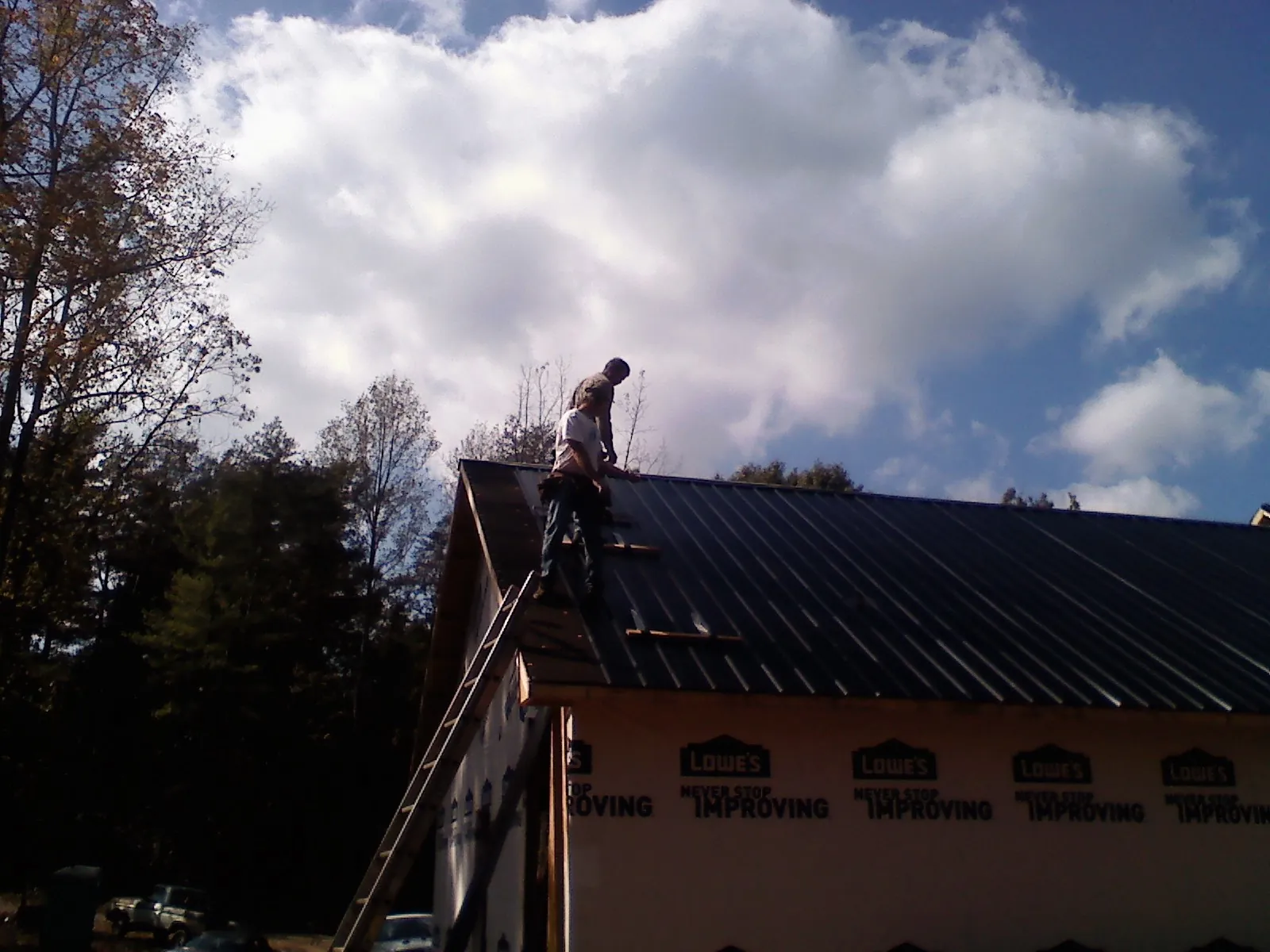 Roofer fastening dark metal panels high against a cloudy sky, from a Roof Inspection job in Rillton