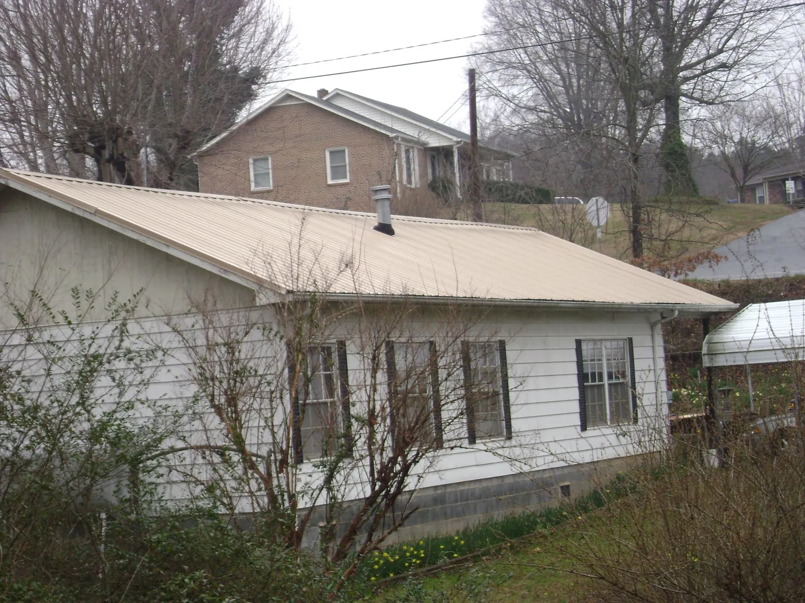 Tan metal roof on a white sided house set into a hillside — Commercial Roofing by Roofing Brothers in Rillton